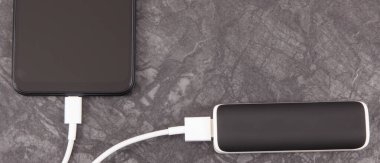 Dış güç bankasının bağlı beyaz fişi olan siyah akıllı telefon. Cep telefonu şarj oluyor. Metin veya yazı için yer
