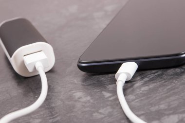 Dış güç bankasının bağlı beyaz fişi olan siyah akıllı telefon. Cep telefonu şarj ediliyor