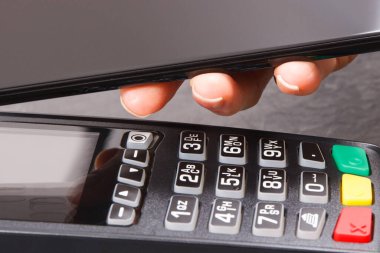 Nakitsiz ödeme yapmak için akıllı telefon ve ödeme terminalini kullanan bir kadın eli. Finans ve bankacılık kavramı