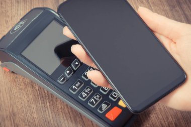 Nakitsiz ödeme yapmak için akıllı telefon ve ödeme terminalini kullanan bir kadın eli. Finans ve bankacılık kavramı