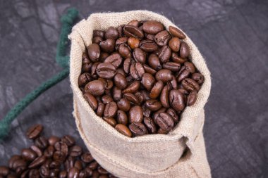 Koyu kavrulmuş kahve tanecikleri beton yapıda jüt torbaya konmuş.