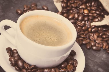 Beyaz fincanda kahve ve kavrulmuş kahve çekirdekleri.