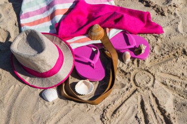 Kumda dinlenmek için güneş ve aksesuar şekli. Hasır şapka, pembe terlikler ve kabarık havlu. Kumsalda tatil zamanı.