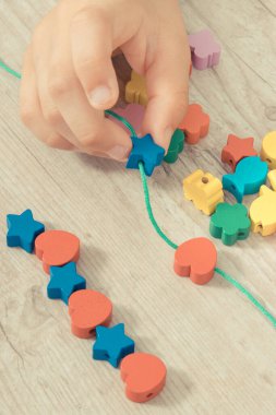 Küçük çocuğun elleri iplikten ve renkli boncuklardan bilezik yapıyor. Çocukların motor becerilerinin, koordinasyonun, yaratıcılığın ve mantıksal düşüncenin geliştirilmesi
