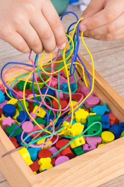İplik çalan çocuğun elleri ve bilezik yapımında kullanılan tahta renkli boncuklar. Çocukların motor becerilerinin ve mantıksal düşüncelerinin gelişimi