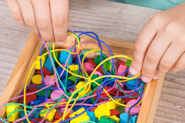 Hands of baby playing thread and wooden colorful beads used to making bracelets. Development of kids motor skills, coordination, creativity and logical thinking