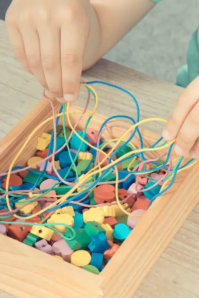 Hands of baby playing thread and wooden colorful beads used to making bracelets. Development of kids motor skills, coordination, creativity and logical thinking