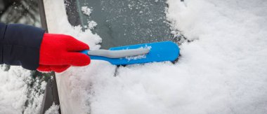 El fırçasıyla araba ve ön camdan kar temizliyor. Ulaşım sırasında kış sorunları