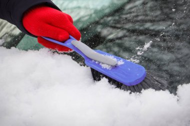 Araba ve ön camlardan kar temizleyen bir kadın eli. Ulaşım sırasında kış sorunları