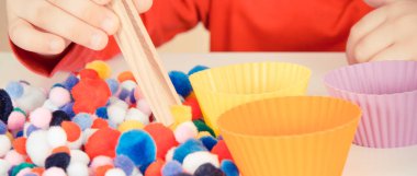 Anaokulu öğrencisi küçük pompodlarla, tahta maşalarla ve fincanlarla oynuyor. Çocukların motor becerilerinin, koordinasyonun, yaratıcılığın ve mantıksal düşüncenin geliştirilmesi