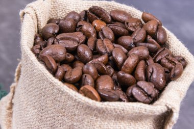 Koyu kavrulmuş kahve çekirdeği yığını beton yapıda jüt torba içinde.