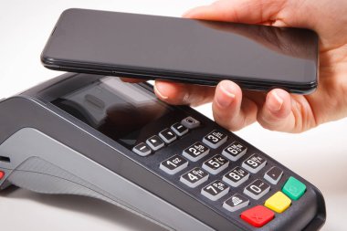 Nakitsiz ödeme yapmak için akıllı telefon ve ödeme terminalini kullanan bir kadın eli. Finans ve bankacılık kavramı