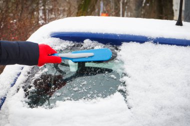 El fırçasıyla araba ve ön camdan kar temizliyor. Ulaşım sırasında kış sorunları