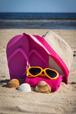 Hasır şapka, pembe terlikler, güneş gözlüğü ve kumsalda kumlu bir havlu. Yaz zamanı dinlenmek için aksesuarlar