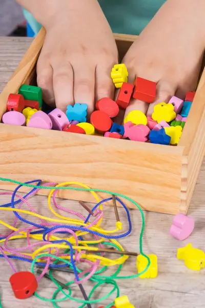 Preschooler playing thread and wooden colorful beads used to making bracelets. Development of kids motor skills, coordination, creativity and logical thinking