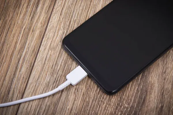 Black smartphone and connected white cable of charger. Mobile phone charging