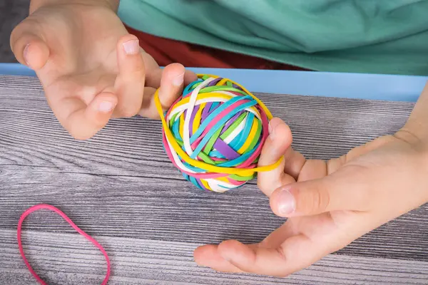 Preschooler hands with ball of colorful rubber bands or erasers. Development of kids motor skills, coordination, creativity and logical thinking