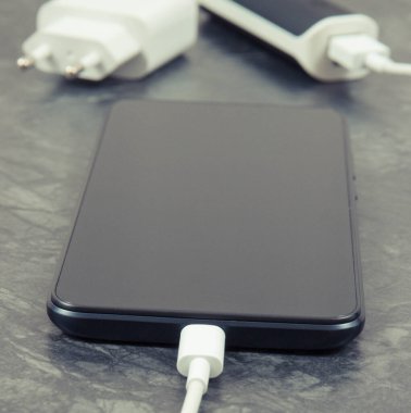 Dış güç bankasının bağlı beyaz fişi olan siyah akıllı telefon. Cep telefonu şarj ediliyor