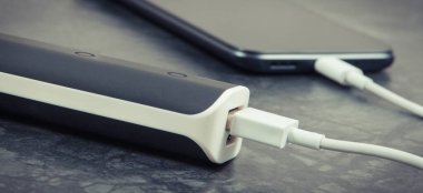 Dış güç bankasının bağlı beyaz fişi olan siyah akıllı telefon. Cep telefonu şarj ediliyor