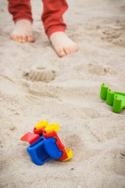 Plastik küçük araba, diğer çocuk oyuncakları ve küçük çocuğun ayakları. Rahatla ya da kumsalda oyna. Yaz ve tatil zamanı