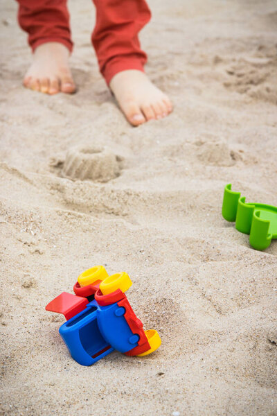 Пластиковая машинка, другие детские игрушки и ноги маленького мальчика. Отдохните или играйте на песке на пляже. Летнее время и отдых