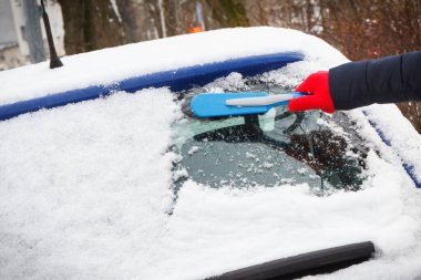 Araba ve ön camlardan kar temizleyen bir kadın eli. Ulaşım sırasında kış sorunları