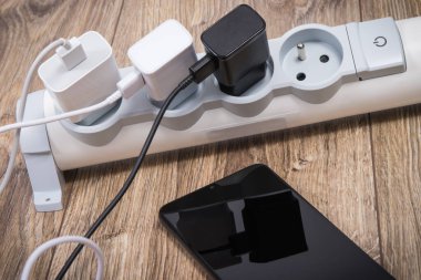 Siyah akıllı telefon, cep telefonu ve elektrik hattına bağlı şarj cihazları. Çeşitli aygıtlar şarj etme kavramı