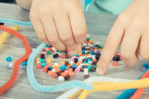 Preschooler hands with creative sticks and colorful beads used to making bracelets. Development of kids motor skills, coordination, creativity and logical thinking