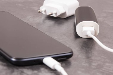 Dış güç bankasının bağlı beyaz fişi olan siyah akıllı telefon. Cep telefonu şarj ediliyor