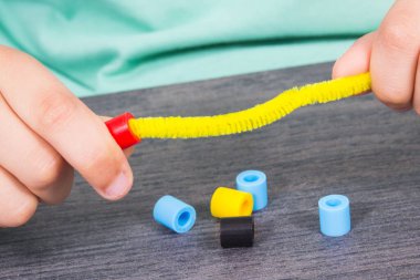 Yaratıcı sopaları ve bilezik yapımında kullanılan renkli boncukları olan anaokulu öğrencilerinin elleri. Çocukların motor becerilerinin, koordinasyonun, yaratıcılığın ve mantıksal düşüncenin geliştirilmesi