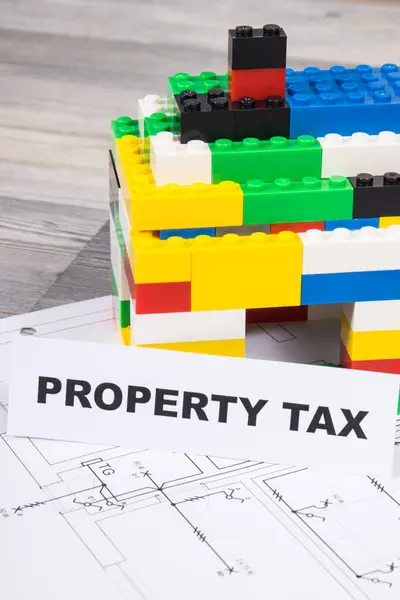 Inscription property tax with small house made of colorful toy blocks. Increasing real estate or luxury taxation. Tax payments