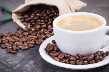 Beyaz cam bardakta kahve ve kavrulmuş kahve çekirdekleri.