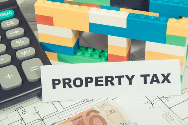 Inscription property tax with small house made of colorful toy blocks, euro banknotes and calculator. Increasing real estate or luxury taxation. Tax payments
