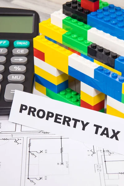 Inscription property tax with small house made of colorful toy blocks and calculator. Increasing real estate or luxury taxation. Tax payments