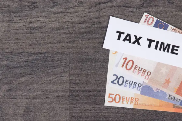 Inscription tax time and euro banknotes. Calculating and paying tax. Wooden background. Place for text