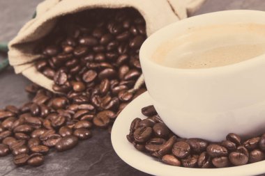 Beyaz cam kahve fincanı ve kavrulmuş koyu kokulu kahve taneleri. Vintage fotoğraf