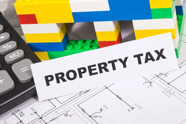Inscription property tax, calculator, small house made of colorful toy blocks and electrical installation plan. Increasing real estate taxation
