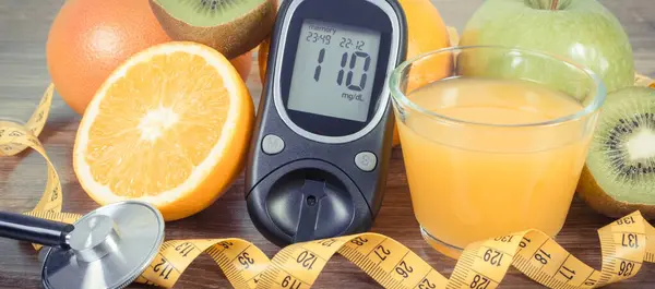 Glucometer with result of sugar level, fresh ripe fruits and orange juice. Source natural minerals and vitamins