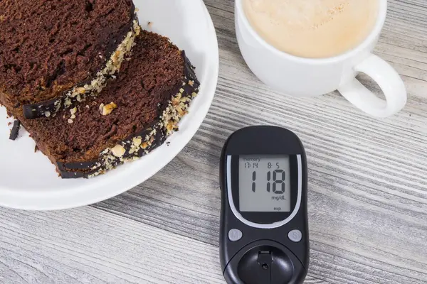 Glucose meter with high result of measurement sugar level, sweet chocolate cake and cup of coffee with milk. Nutrition during diabetes concept