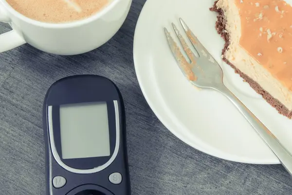 Glucometer using for sugar level control, portion of fresh baked sweet cheesecake and cup of coffee with milk. Nutrition during diabetes