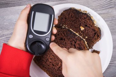 Glikoz ölçer ve çikolatalı pasta tutan bir çocuk eli. Diyabet sırasında şeker seviyesini ölçmek ve kontrol etmek