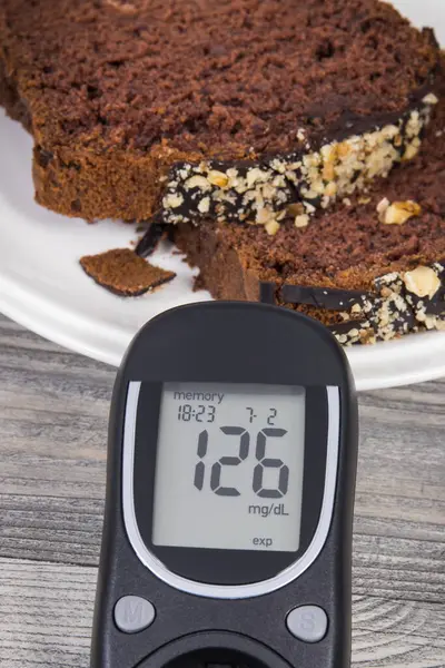 Glucose meter with high result of measurement sugar level, sweet chocolate cake. Nutrition during diabetes concept