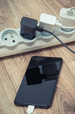 Siyah akıllı telefon, cep telefonu ve elektrik hattına bağlı şarj cihazları. Çeşitli aygıtlar şarj etme kavramı