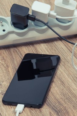 Siyah akıllı telefon, cep telefonu ve elektrik hattına bağlı şarj cihazları. Çeşitli aygıtlar şarj etme kavramı