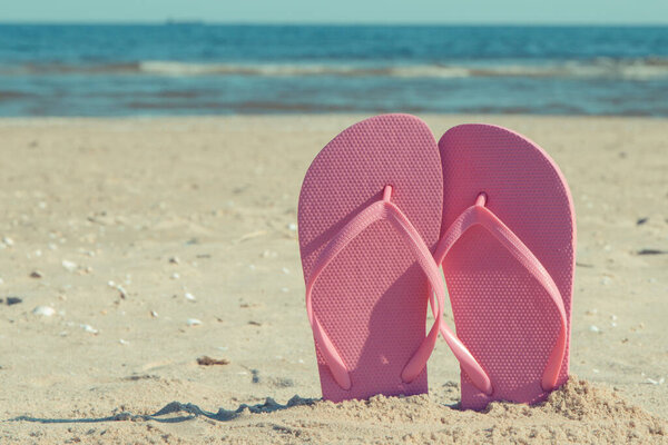 Pink slippers on sand at beach. Accessories for relax in summer time