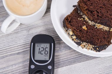 Şekerin ölçülmesi sonucu glikoz ölçer, çikolatalı tatlı kek ve sütlü kahve. Diyabet sırasında şeker seviyesini ölçmek ve kontrol etmek