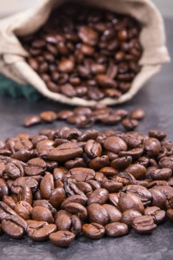 Koyu kavrulmuş kahve çekirdeği yığını beton yapıda jüt torba içinde.