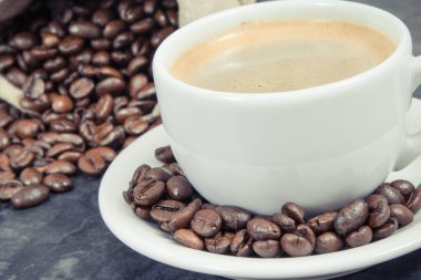 Beyaz fincanda kahve ve kavrulmuş kahve çekirdekleri.