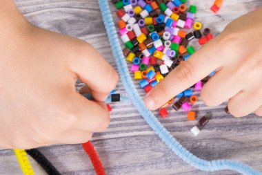 Yaratıcı sopaları ve bilezik yapımında kullanılan renkli boncukları olan anaokulu öğrencilerinin elleri. Çocukların motor becerilerinin, koordinasyonun, yaratıcılığın ve mantıksal düşüncenin geliştirilmesi