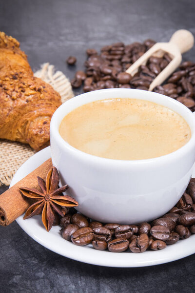 Coffee in white cup with star of anise and cinnamon stick and fresh baked croissant